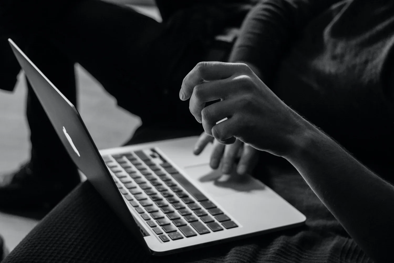 A person is using a laptop, with their right hand hovering over the keyboard and their left hand resting on the laptop's surface.